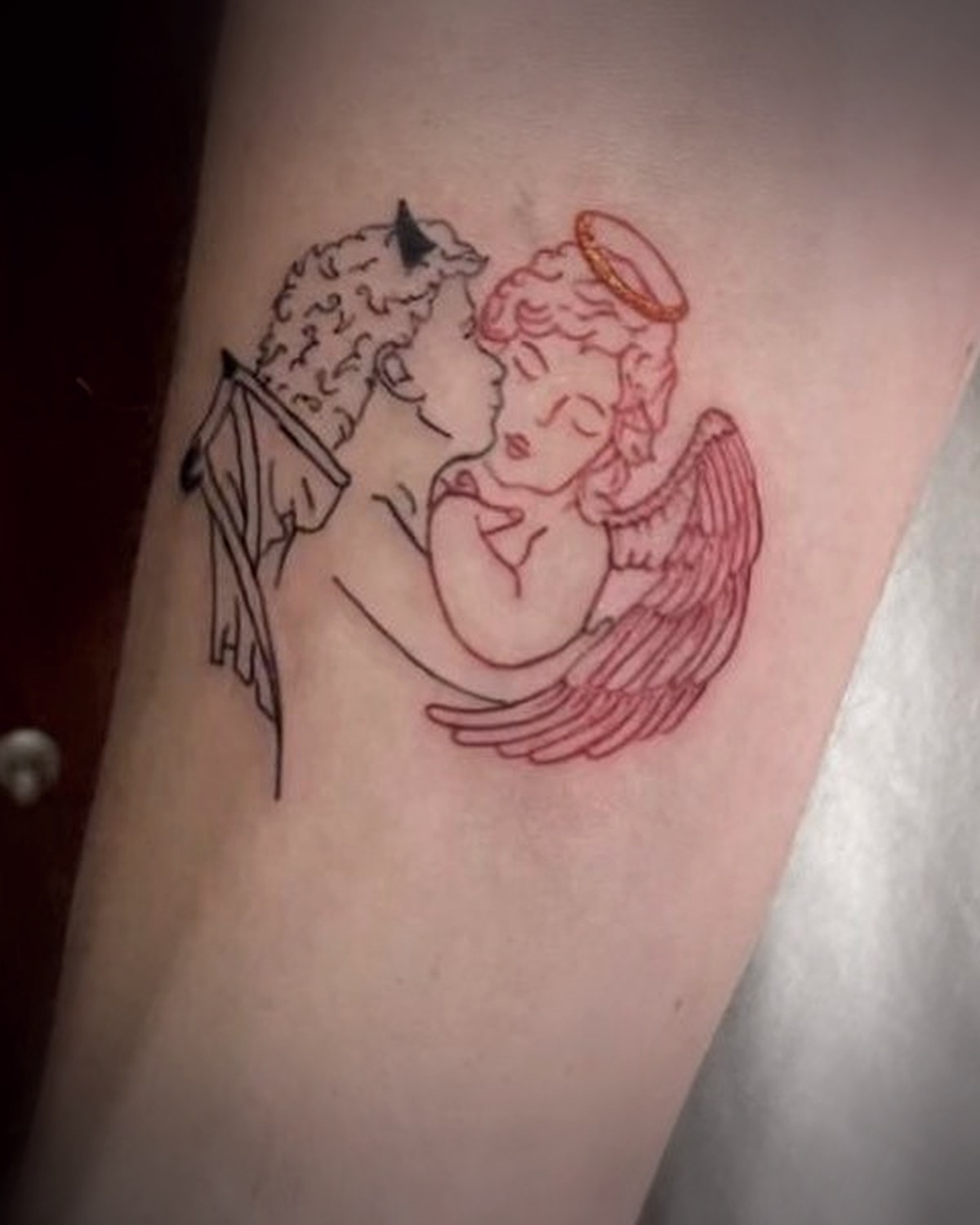 Ángel y diablo en línea fina con tinta roja en el antebrazo