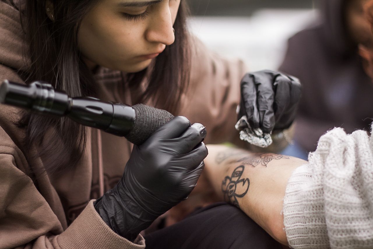 Natalia Rivera tatuando con guantes negros y máquina de tatuaje